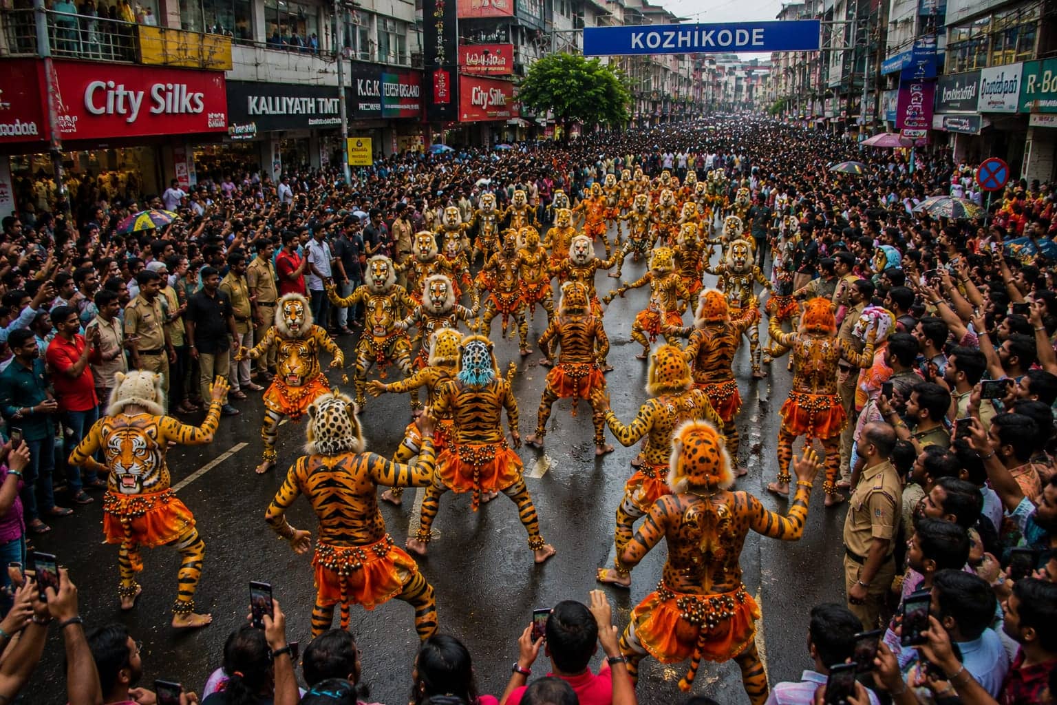 Tiger dancers parade down a street lined with shopfronts as onlookers crowd the pavement.
